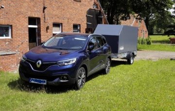 Auto mit Anhänger vor rotem Backsteinhaus