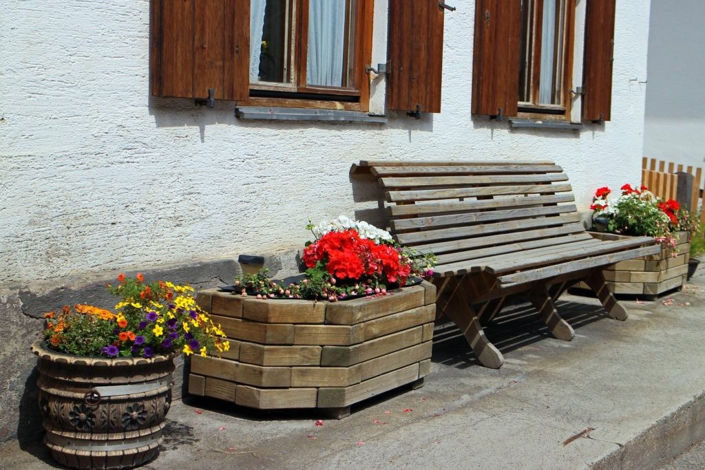 Holzbank mit bunten Blumen vor weißem Bauernhaus