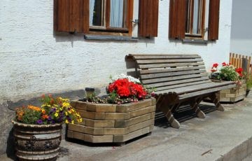 Holzbank mit bunten Blumen vor weißem Bauernhaus